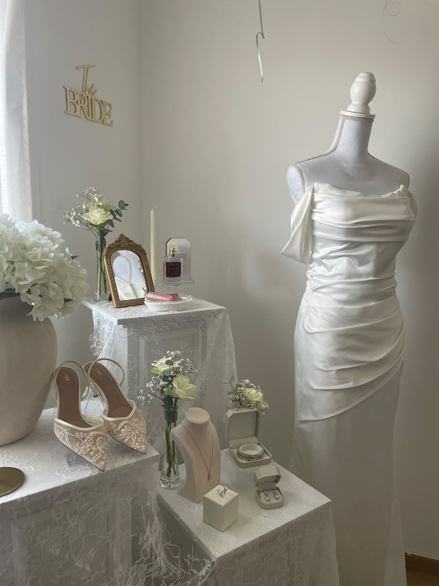 Robe de mariée sur un buste, escarpins brodés, bijoux et fleurs blanches préparés pour la mariée